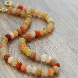 May include: A multi-colored beaded necklace with gold clasps. The beads are shades of orange, yellow, and pink.