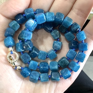 Pode incluir: Um colar de pedras preciosas azuis com contas quadradas e um fecho de ouro. O colar é feito com um cordão azul.