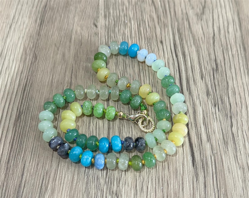 May include: A beaded necklace with a variety of colorful beads. The beads are in shades of green, blue, yellow, and clear. The necklace has a gold-colored clasp. The beads are approximately 0.5 cm in diameter.