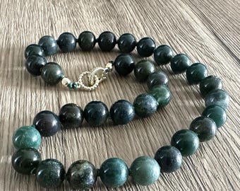 Puede incluir: Un collar de cuentas de ágata verde con un cierre de oro. Las cuentas son redondas y tienen un aspecto moteado.