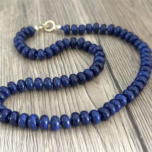 Könnte beinhalten: Eine Halskette aus dunkelblauen runden Perlen mit einem goldenen Verschluss.