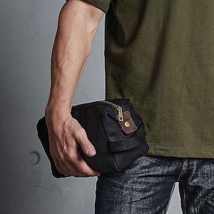 May include: A black canvas wash bag with a brown leather trim and a zip fastening.