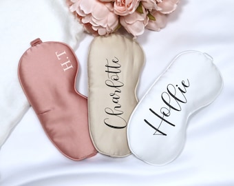 May include: Three satin sleep masks with personalized names. The masks are in pink, beige, and white.