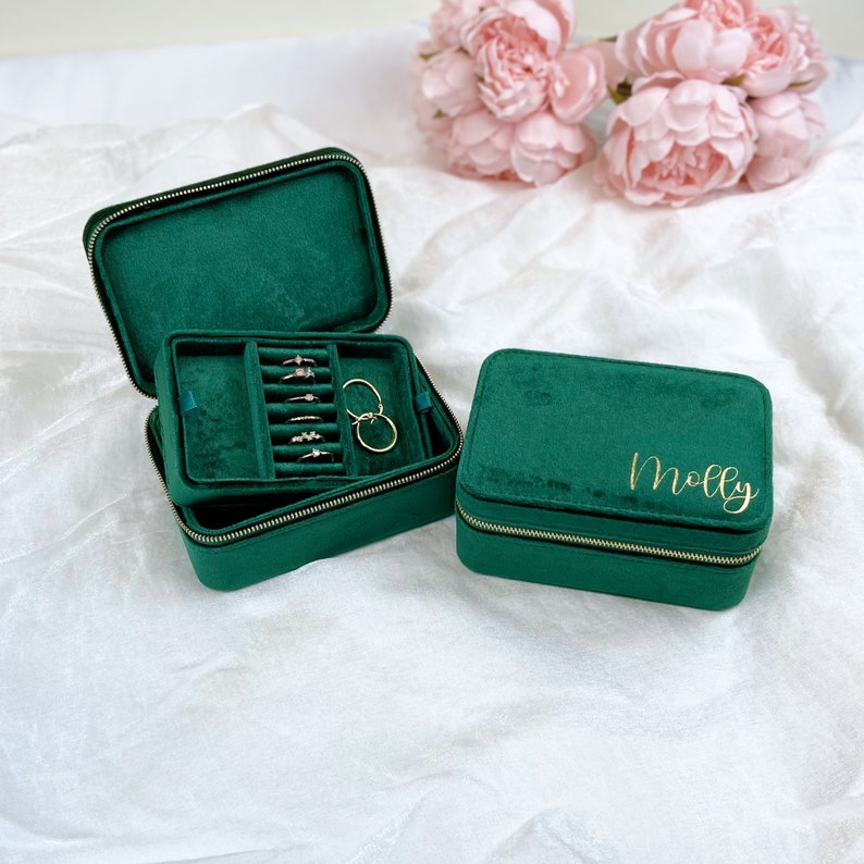 May include: Two green velvet jewelry boxes with gold zippers. The smaller box has the name "Molly" written in gold script on the top. The larger box is open and has a compartment for rings and earrings.