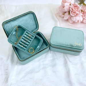 May include: Two teal velvet jewelry boxes with gold zippers. The larger box is open and has a compartment for necklaces and earrings. The smaller box is closed and has the name "Jade" written on it in gold lettering.