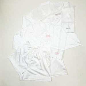 May include: White satin pajama sets, including long-sleeved button-down shirts and shorts. One shirt is embroidered with "Mrs. Cox", another with "TPR", and the cuffs with dates. A luxurious and personalized sleepwear collection.