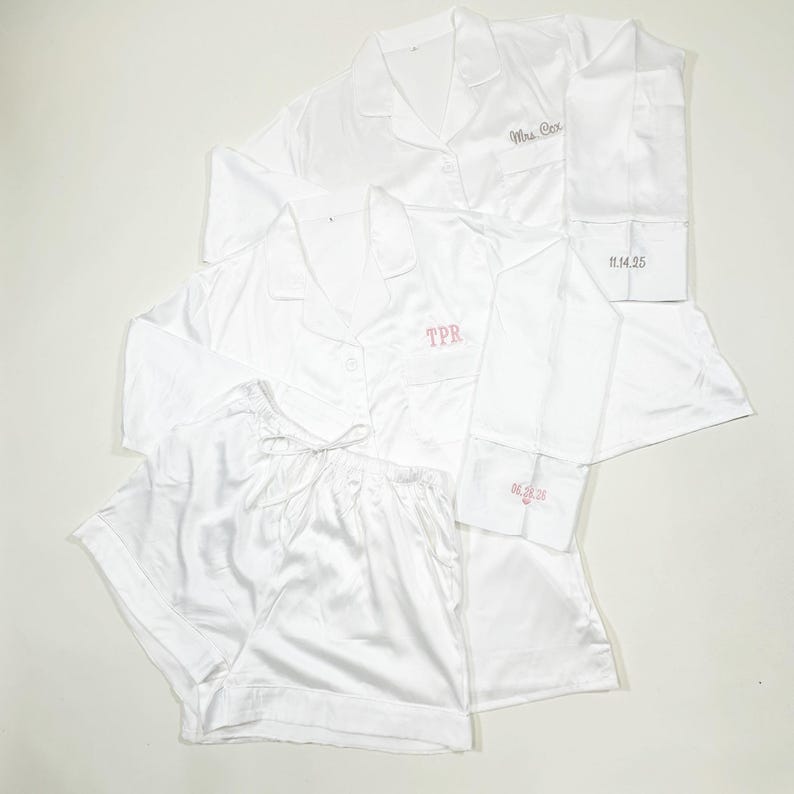 May include: White satin pajama sets, including long-sleeved button-down shirts and shorts. One shirt is embroidered with "Mrs. Cox", another with "TPR", and the cuffs with dates. A luxurious and personalized sleepwear collection.