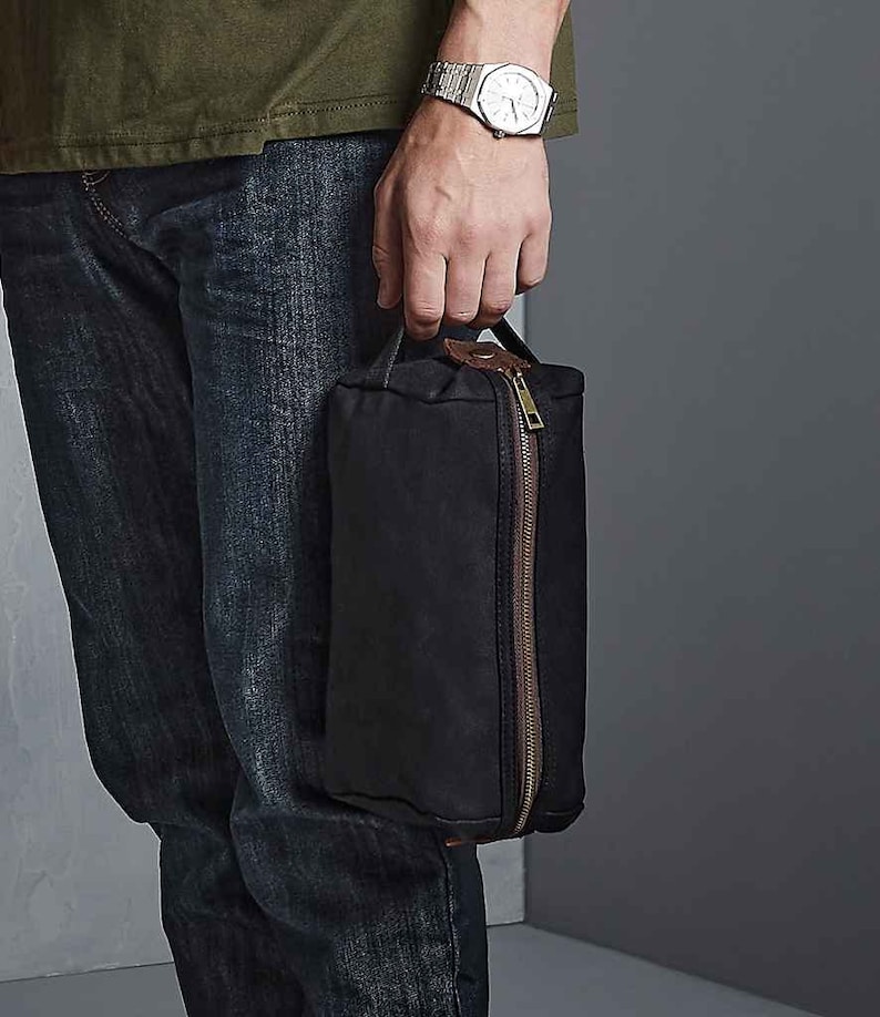 May include: A black canvas wash bag with a brown leather handle and zip. The bag is approximately 8 inches tall and 5 inches wide.