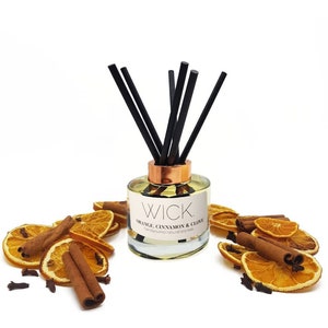 May include: A clear glass diffuser bottle with black reeds and a copper-colored collar. The label reads "WICK. ORANGE, CINNAMON & CLOVE." Dried orange slices, cinnamon sticks, and cloves surround the bottle, creating a warm, inviting aesthetic.