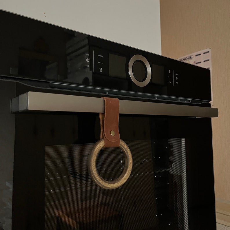 May include: A black oven with a brown leather ring hanging from the handle. The ring is made of wood and has a natural finish.