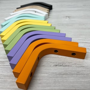 Op de afbeelding: Een set van 12 kleurrijke houten hoekbeugels, gerangschikt in een regenboogpatroon. De beugels zijn geverfd in verschillende tinten blauw, groen, geel, oranje en paars. De beugels zijn gemaakt van hout en hebben een gladde afwerking.