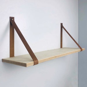 May include: A light wood shelf with two brown leather straps attached to the wall. The shelf is empty.