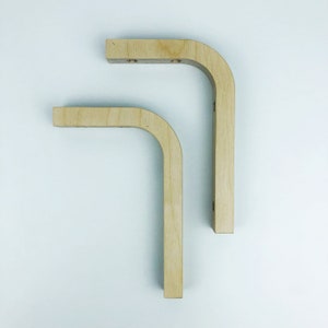 May include: Two wooden shelf brackets with a rounded corner design. The brackets are made of light wood and are unfinished.
