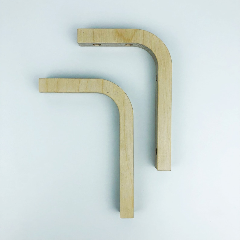 May include: Two wooden shelf brackets with a rounded corner design. The brackets are made of light wood and are unfinished.