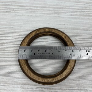 May include: A dark brown wooden ring with a diameter of approximately 7.5 cm. The ring is measured with a ruler.