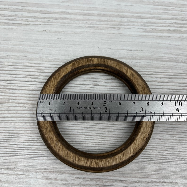May include: A dark brown wooden ring with a diameter of approximately 7.5 cm. The ring is measured with a ruler.