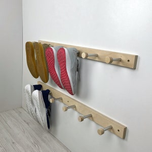 May include: A wooden shoe rack with five hooks mounted on a white wall. The rack has two shelves, and there are four pairs of shoes hanging on the hooks and two pairs of shoes on the shelves.