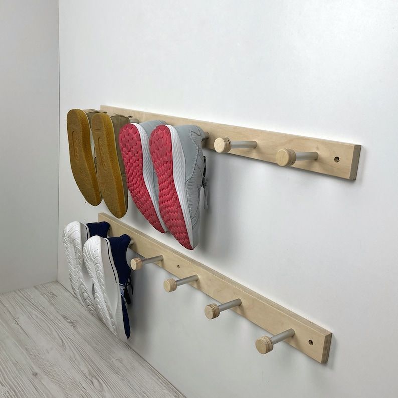 May include: A wooden shoe rack with five hooks mounted on a white wall. The rack has two shelves, and there are four pairs of shoes hanging on the hooks and two pairs of shoes on the shelves.