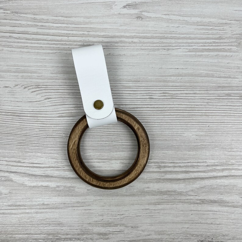 May include: A white leather strap with a brass button attached to a wooden ring. The ring is brown and has a smooth finish.