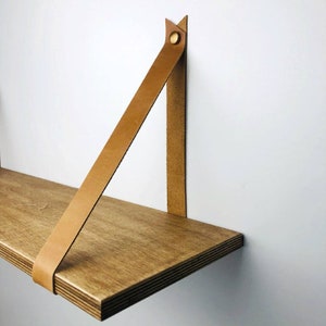 May include: A wooden shelf with a brown leather strap attached to the wall. The strap is secured with a brass button.