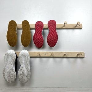May include: A wooden shoe rack with six hooks and five pairs of shoes. The shoes are a mix of red, yellow, and white.