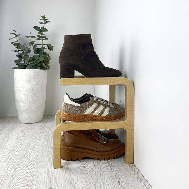 Puede incluir: Un zapatero de madera de tres niveles, que contiene un par de botines marrones, un par de zapatillas blancas y marrones y un par de mocasines marrones.
