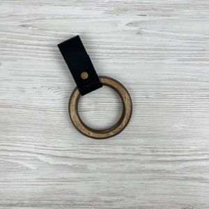 May include: A wooden ring with a black leather strap and a brass button. The ring is made of dark wood and has a smooth finish.