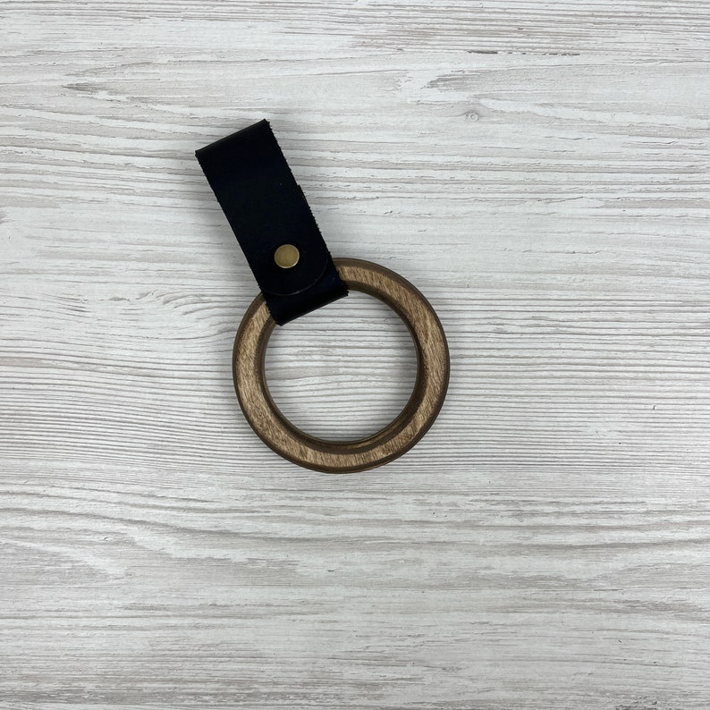 May include: A wooden ring with a black leather strap and a brass button. The ring is made of dark wood and has a smooth finish.