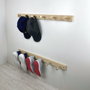 May include: A wooden wall-mounted rack with hooks for hanging hats and shoes. Two baseball caps hang on the top rack, one blue and one black. Three pairs of shoes hang on the bottom rack, one pair white, one pair red, and one pair grey.