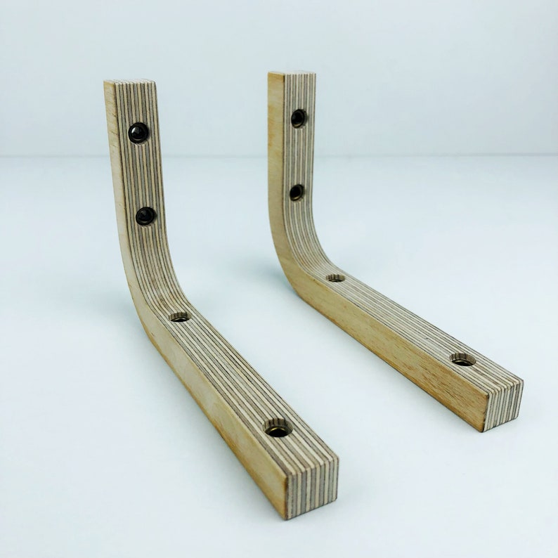 May include: Two wooden shelf brackets with a light brown finish and a curved design. The brackets have multiple screw holes for mounting.