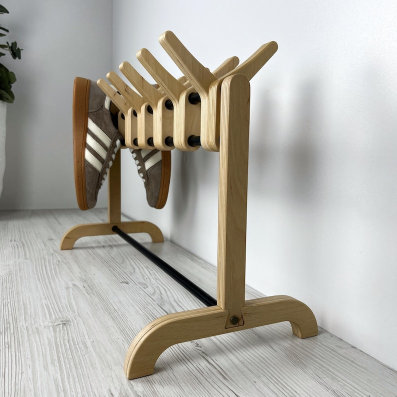 May include: A wooden shoe rack with a black metal bar and multiple angled slots for storing shoes. The rack is made of light wood and has a simple, modern design.