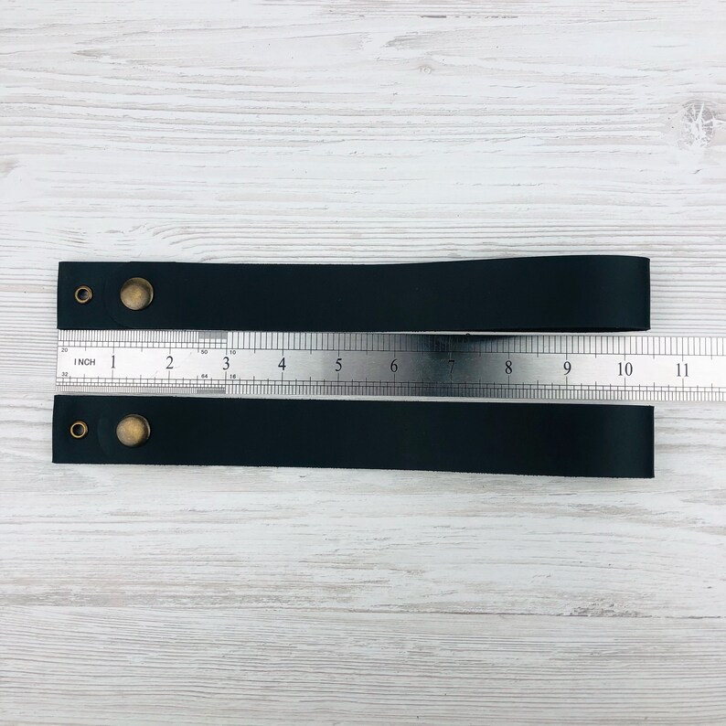 Pu&ograve; includere: Due cinturini in pelle nera con rivetti in ottone e un righello che misura 25,4 cm di lunghezza.
