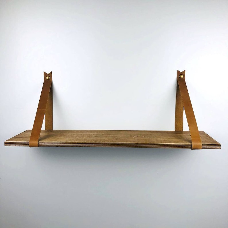 May include: A wooden shelf with brown leather straps attached to the wall. The shelf is made of natural wood and has a rustic look.