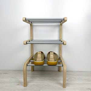 Pu&ograve; includere: Uno scarpiera in legno con due ripiani e binari in metallo argentato. Due paia di scarpe beige sono sullo scaffale inferiore.