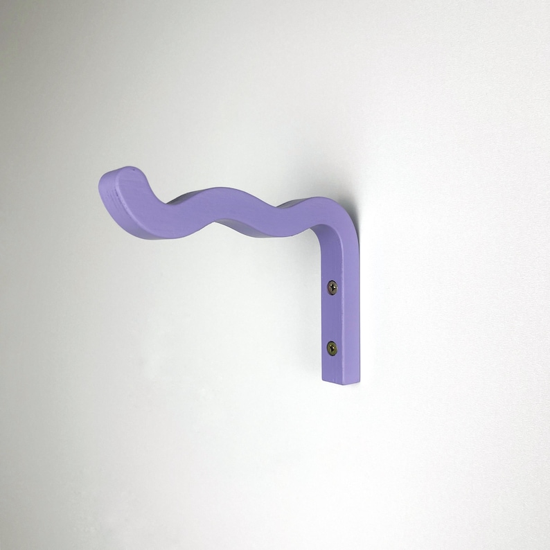 May include: A light purple wall-mounted hook with a wavy design. The hook is made of wood and has two screws.