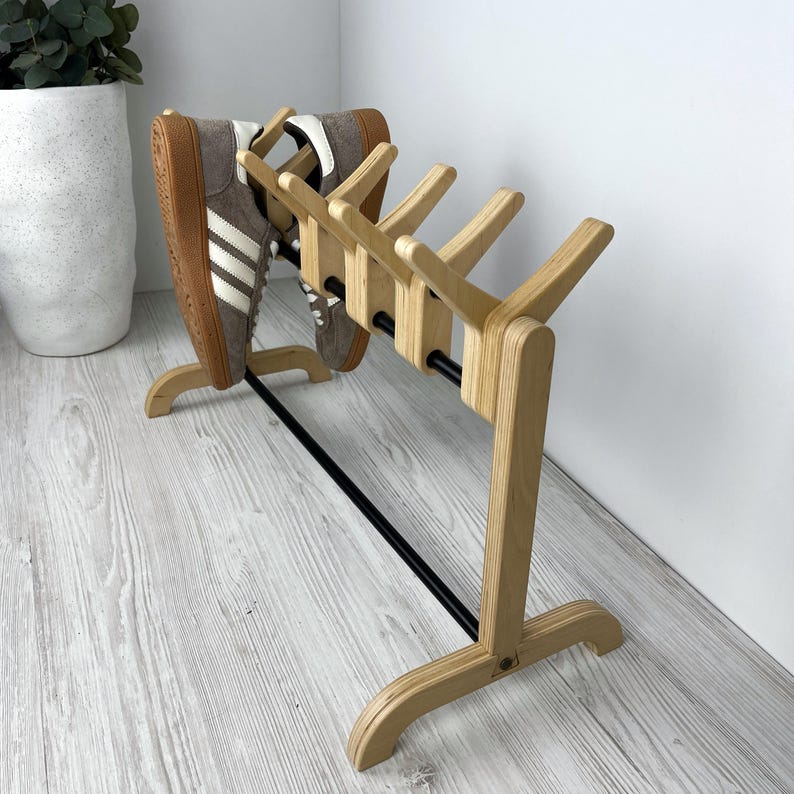May include: A wooden shoe rack with a black metal bar. The rack has six curved wooden pegs for holding shoes. Two pairs of shoes are hanging on the rack.