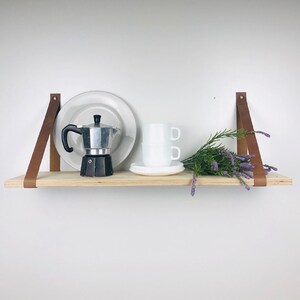 May include: A wooden shelf with brown leather straps, a white plate, a white cup, a silver coffee pot, and a bouquet of purple flowers.