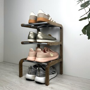 Pu&ograve; includere: Uno scarpiera in legno con quattro ripiani e binari in metallo argentato. La scarpiera &egrave; piena di scarpe, tra cui sneakers, mocassini e sandali.
