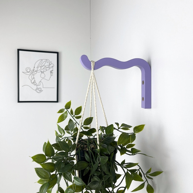 May include: A light purple wooden wall-mounted plant hanger with a curved design. A hanging plant with green leaves is suspended from the hanger.