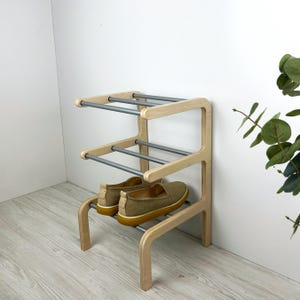 Pu&ograve; includere: Uno scarpiera in legno con tre ripiani e binari in metallo argentato. La scarpiera ha una finitura in legno chiaro e si trova su un pavimento in legno chiaro.