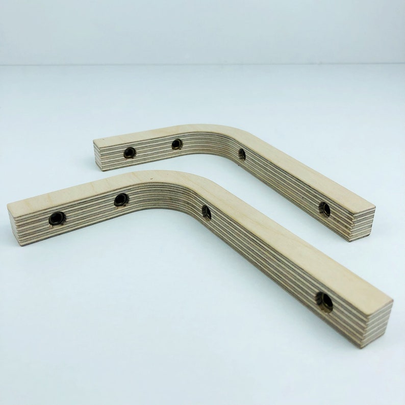 May include: Two wooden shelf brackets with a curved shape and multiple holes for mounting. The brackets are made of light-colored wood with a natural grain.