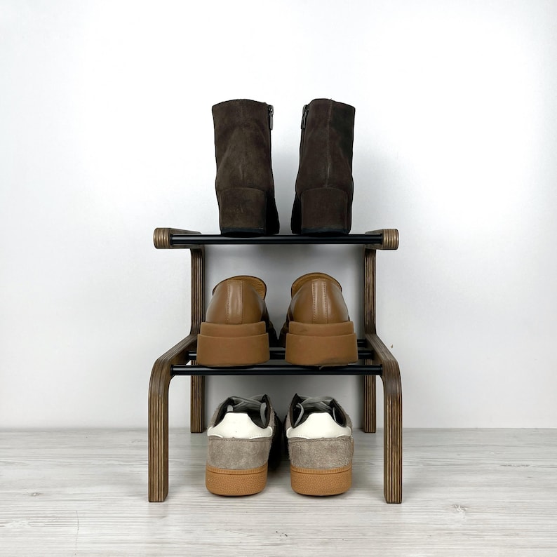Puede incluir: Un zapatero de madera de dos niveles con estantes de metal negro. El estante superior tiene dos botines marrones y el estante inferior tiene dos pares de zapatillas marrones y grises.