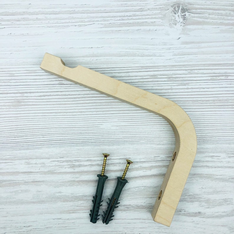 Puede incluir: Un soporte de pared en forma de L hecho de madera clara, con una esquina curva y una muesca circular en el extremo superior. El soporte incluye dos orificios pretaladrados para el montaje y viene con dos tornillos dorados y tacos de pl&aacute;stico.