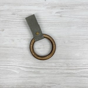 May include: A wooden ring with a gray leather strap. The ring is made of dark wood and has a smooth finish. The strap is attached to the ring with a metal button.