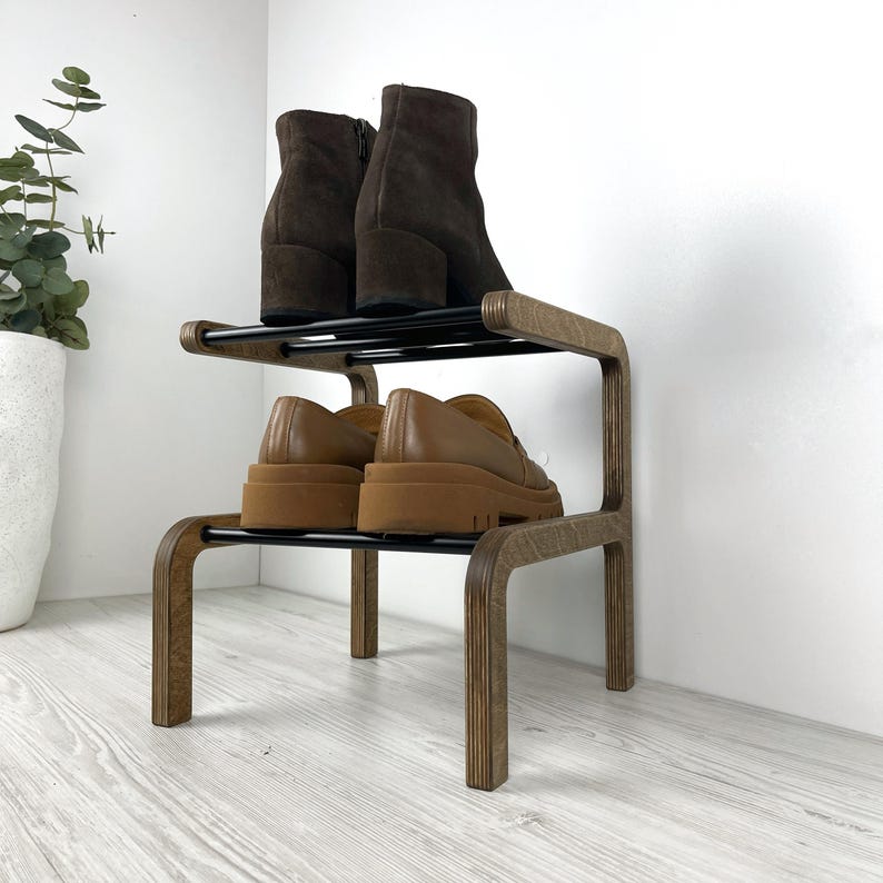 Puede incluir: Un zapatero de madera de dos niveles con soportes de metal negro. El estante est&aacute; hecho de madera marr&oacute;n claro y tiene un acabado de madera natural. El estante contiene dos pares de zapatos, un par de botines marrones de tobillo y un par de mocasines marrones.