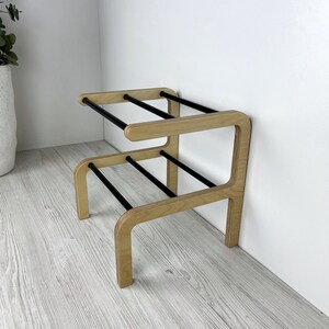 Puede incluir: Un zapatero de madera con barras de metal negro. El zapatero tiene dos estantes y est&aacute; dise&ntilde;ado para ser montado en una pared.