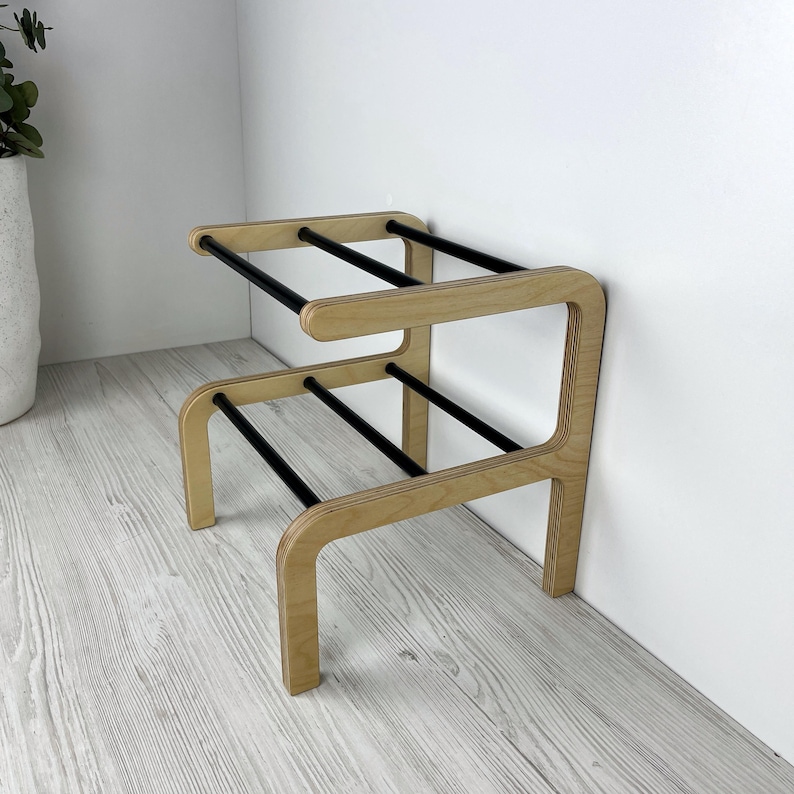 Puede incluir: Un zapatero de madera con barras de metal negro. El zapatero tiene dos estantes y est&aacute; dise&ntilde;ado para ser montado en una pared.