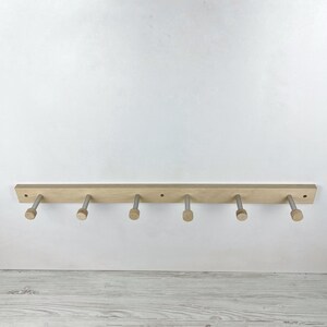 May include: A wooden wall-mounted coat rack with six silver hooks. The rack is made of light wood and has a natural finish.