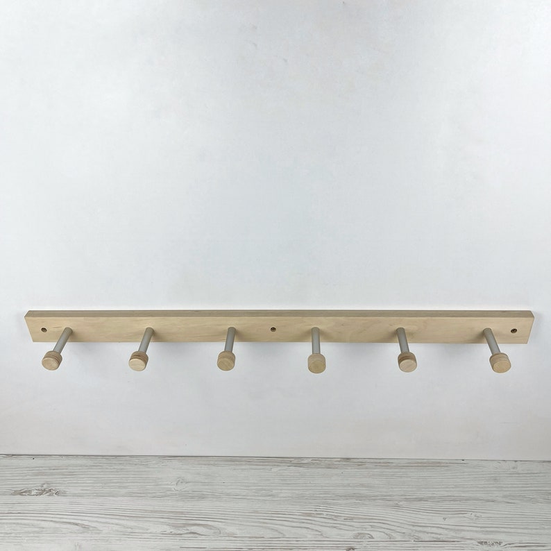 May include: A wooden wall-mounted coat rack with six silver hooks. The rack is made of light wood and has a natural finish.