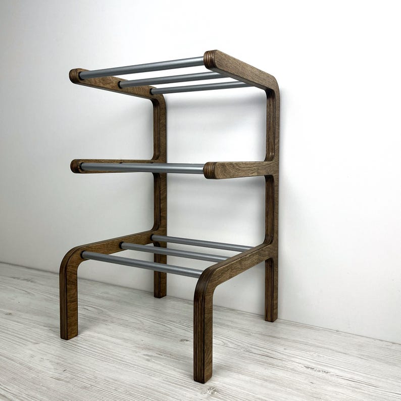 Pu&ograve; includere: Uno scarpiera in legno con tre ripiani e binari in metallo argentato. La scarpiera ha una macchia marrone scuro e gambe arrotondate.